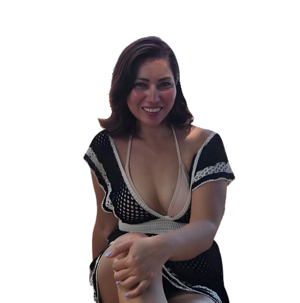 Portrait of Neslyn Sellers seated in a sun-dappled garden, surrounded by lush greenery. She smiles gently, hands folded in her lap, radiating calm and warmth. The setting is tranquil, with soft natural light. 3:2 aspect ratio.