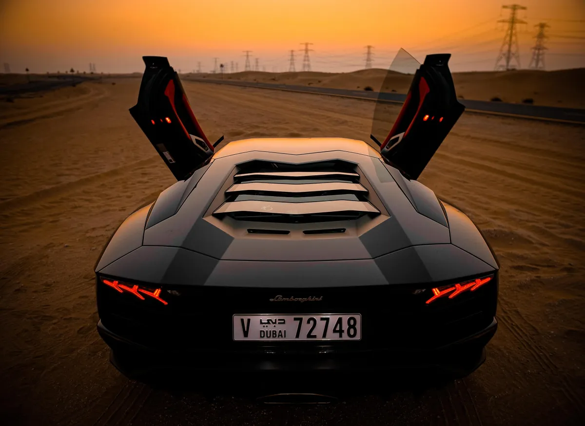 Lamborghini Aventador in Dubai desert at sunset, displaying open scissor doors and sleek design.