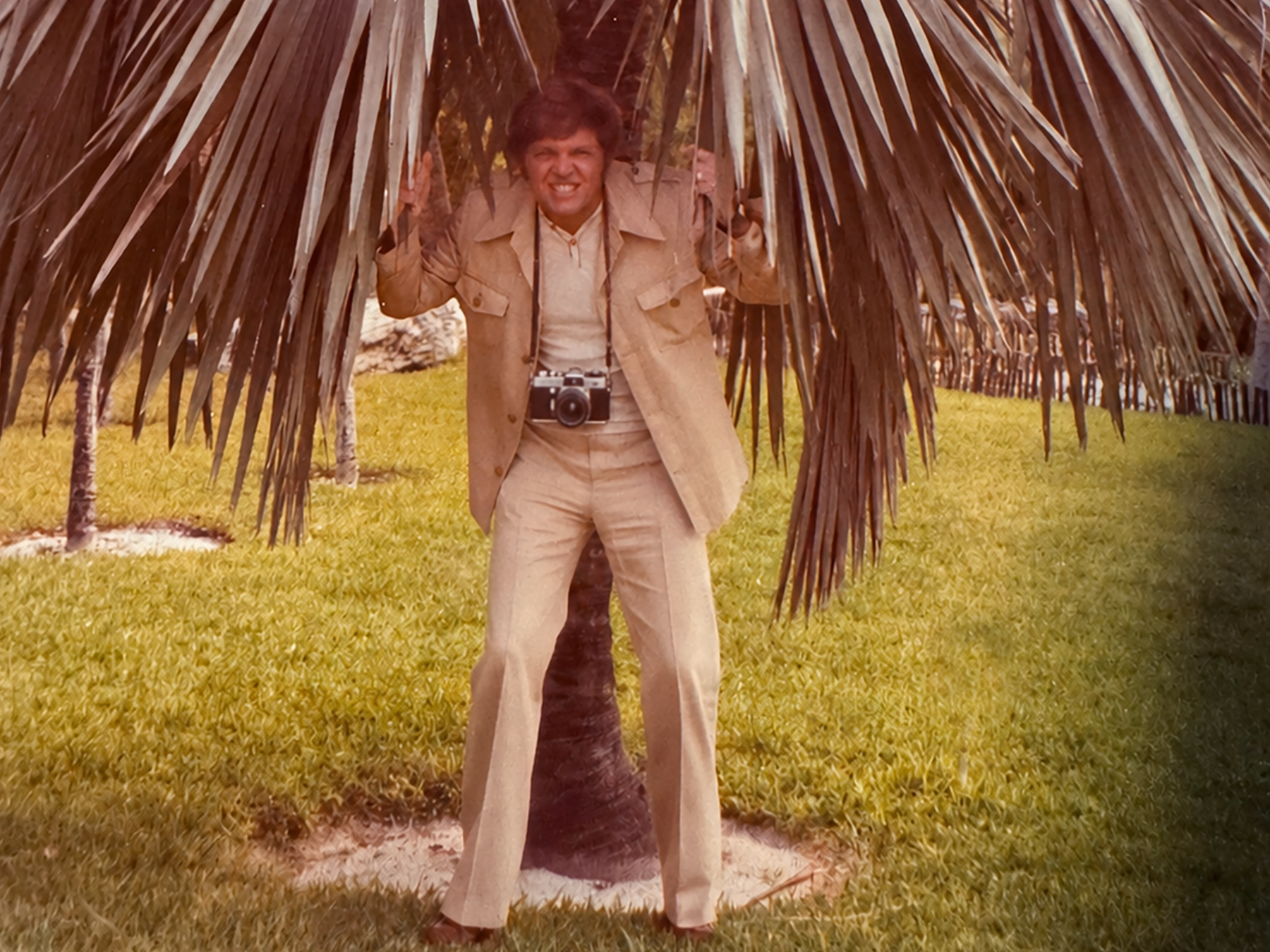 Man wearing a camera on a strap standing beneath palm tree