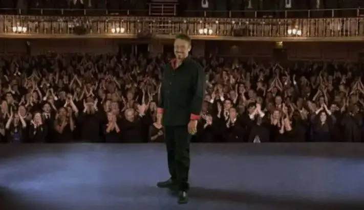 Elijah Edwards performing on stage in a theater with a live audience visible in the background