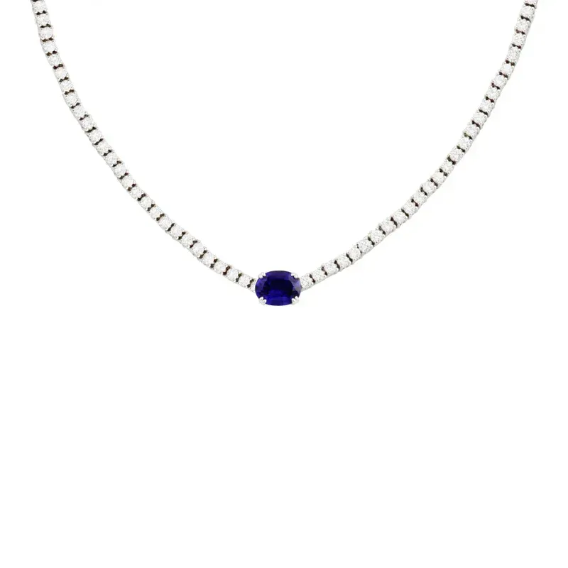 An 18k white gold tennis necklace designed with an oval-shaped sapphire charm