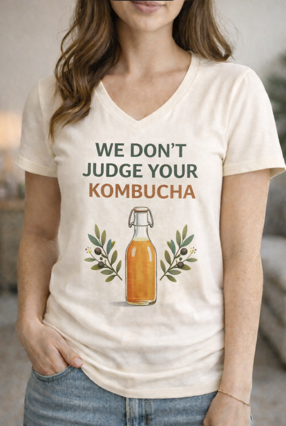 Woman wearing a cream-colored V-neck T-shirt that says “We don’t Judge Your Kombucha,” representing The Christian Wellness Club