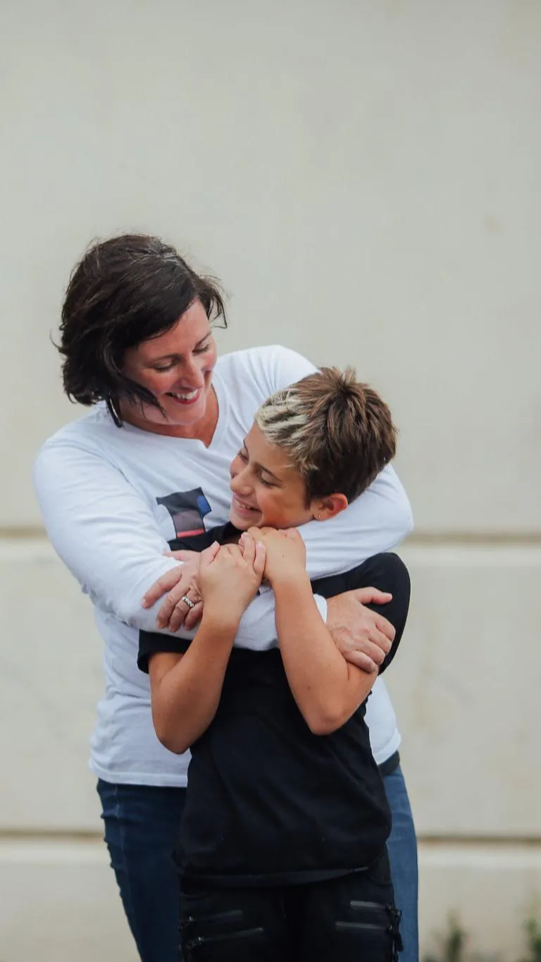 A mother and son smiling at one another in a loving embrace.