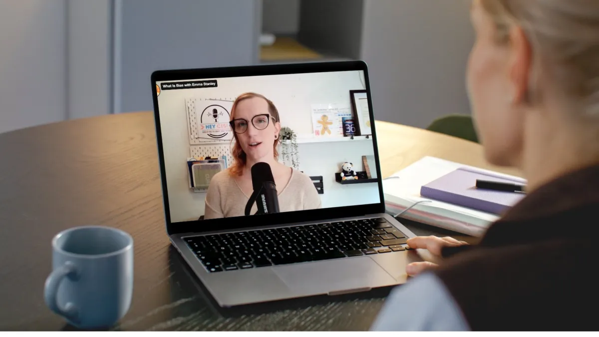 Person working on a laptop watching a video of a woman talking into a microphone