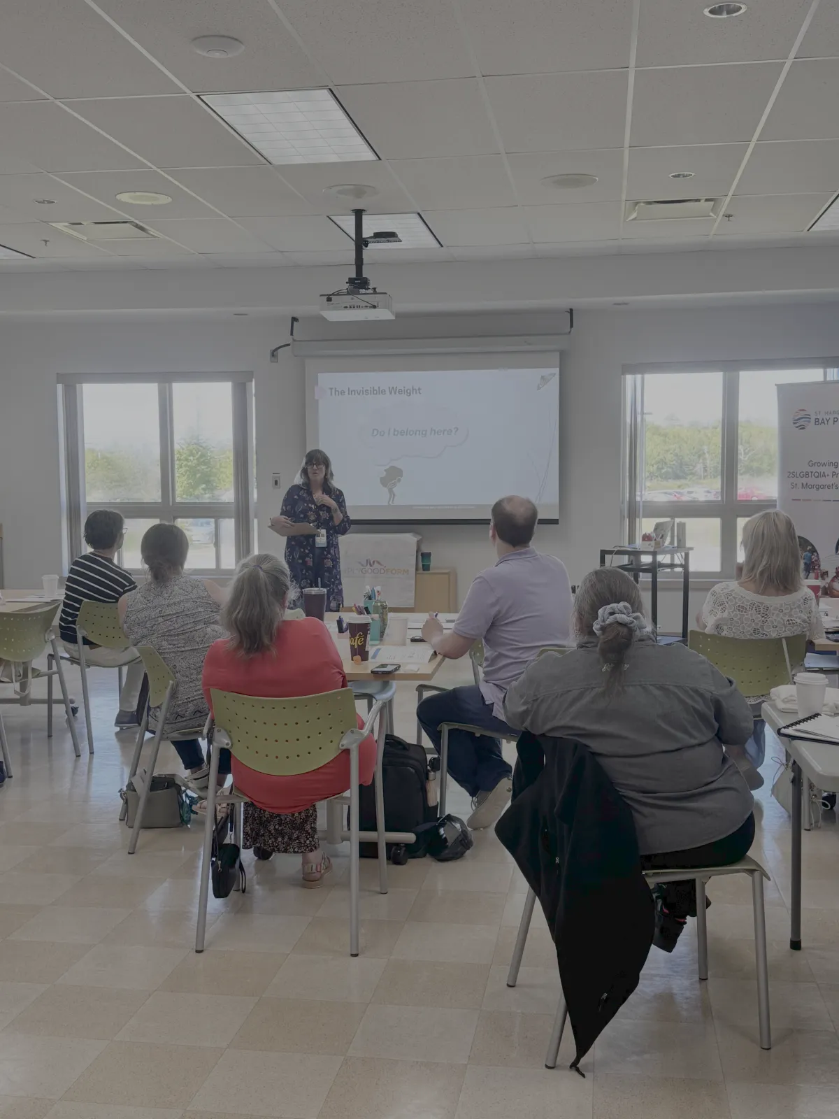 A person standing in front of a screen giving a presentation to a room of seated people. An example of group workshops and coaching with Cynthia