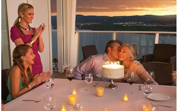 A family celebrating a birthday with cake and candles on their cruise ship balcony.