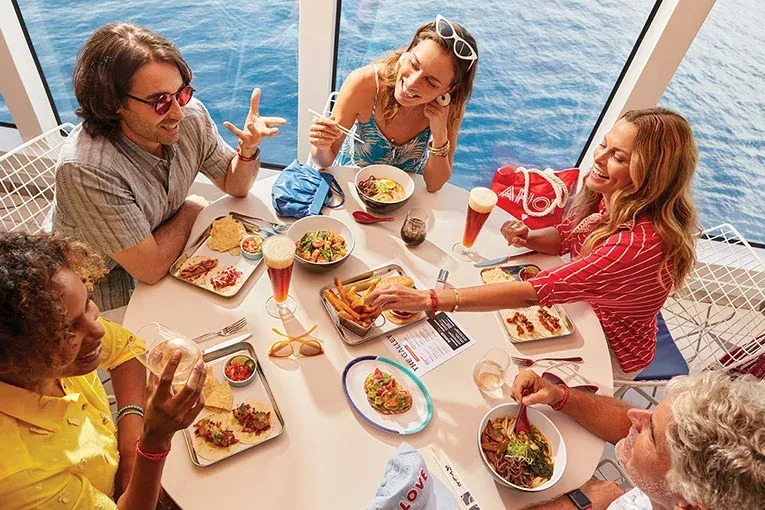 Five young adults sitting around a table eating, overlooking the ocean on a cruise ship
