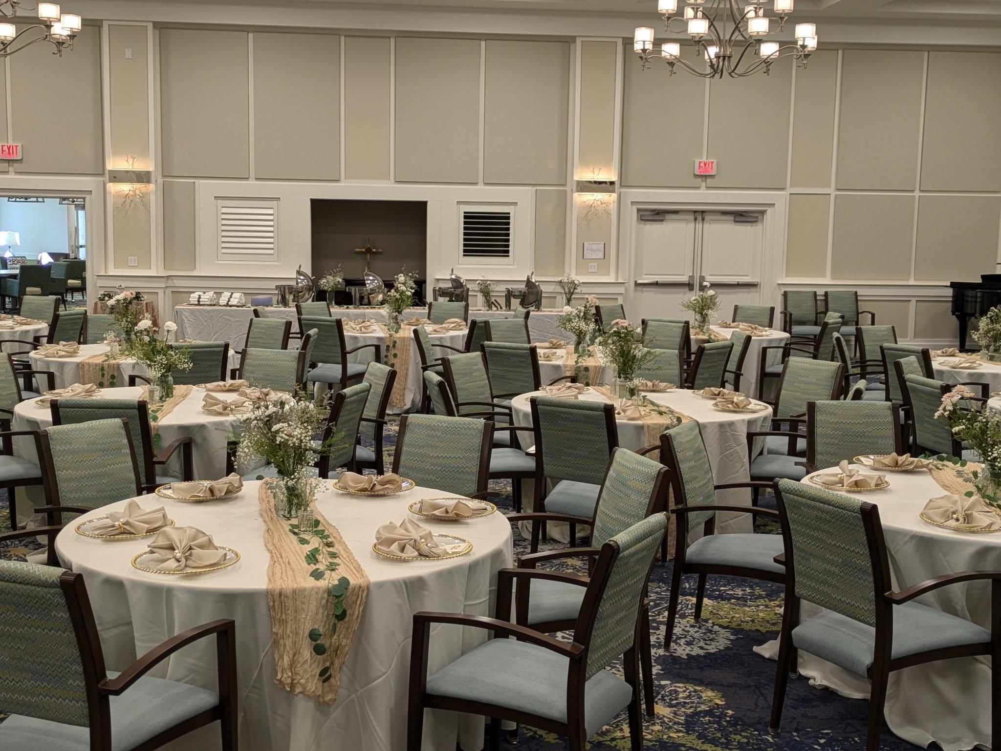 Elegant dining setup for boutique weddings and celebrations, featuring round tables dressed in white linens with decorative centerpieces of fresh flowers, intertwined greenery, and intricately folded napkins, set in a stylish venue with soft lighting and a welcoming atmosphere.