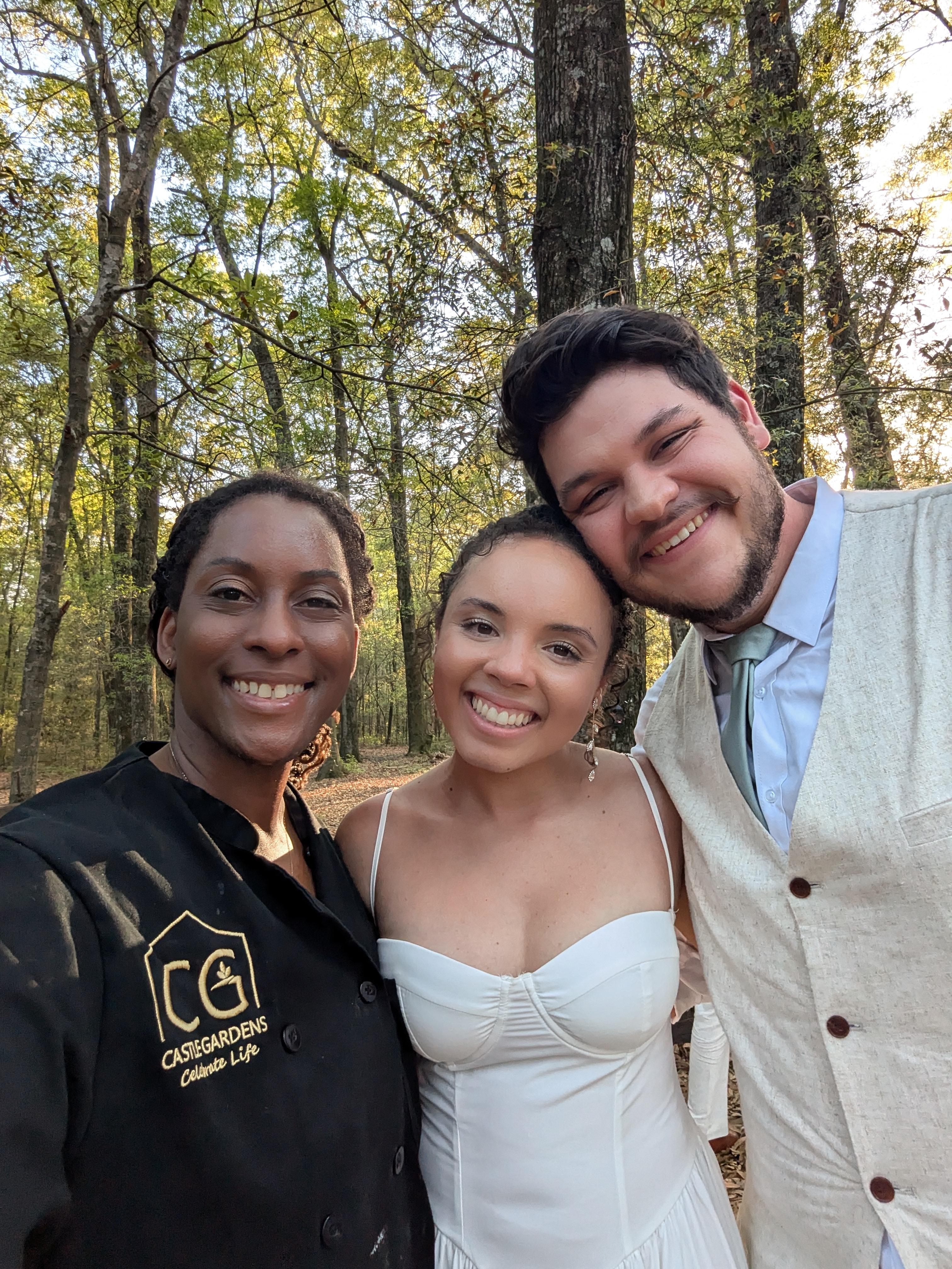 Smiling wedding couple with event coordinator in a forest setting, showcasing Castle Gardens ILM's personalized event planning and catering services.