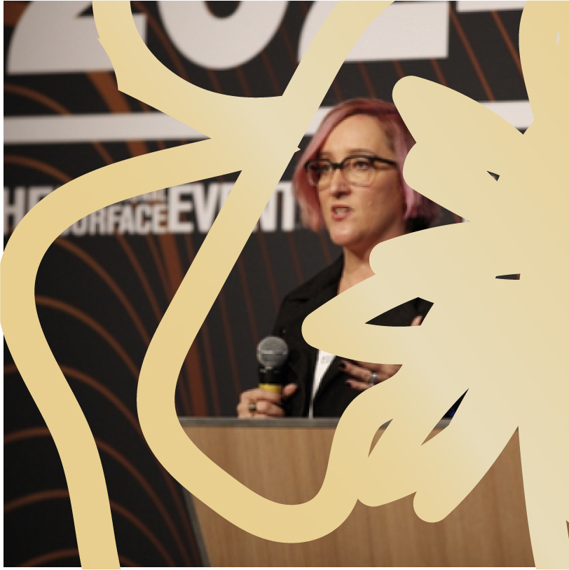 Woman speaking into a microphone during a presentation, standing in front of a branded backdrop.