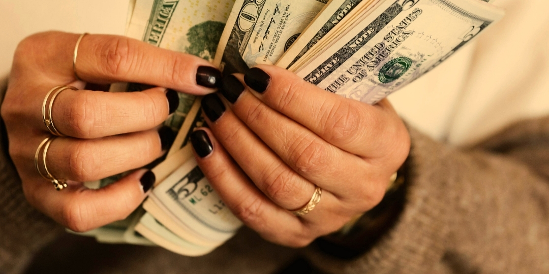 Close-up of hands with dark nail polish holding and counting U.S. dollar bills.