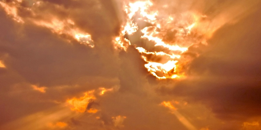 Dramatic golden sunset with sun rays breaking through clouds in a glowing sky.