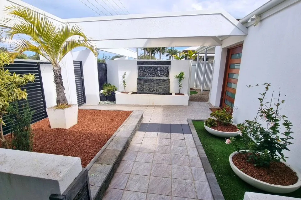 Low-maintenance landscaped courtyard with paved pathway, raised garden beds, garden edging, mulch and tropical plants