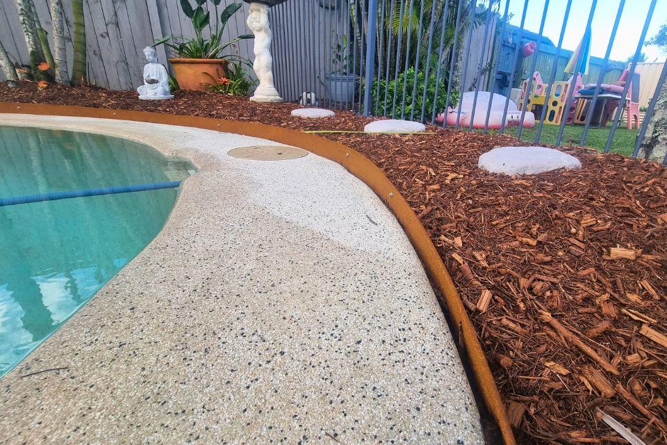 Poolside garden with curved steel edging, mulch and stepping stones