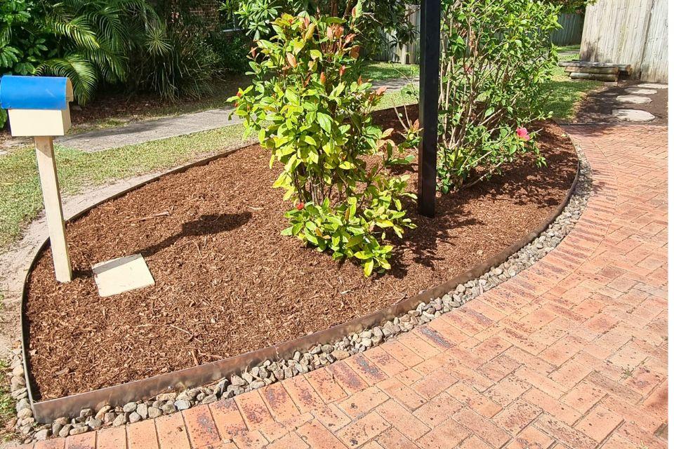 Freshly mulched garden bed with stone edging along a brick pathway