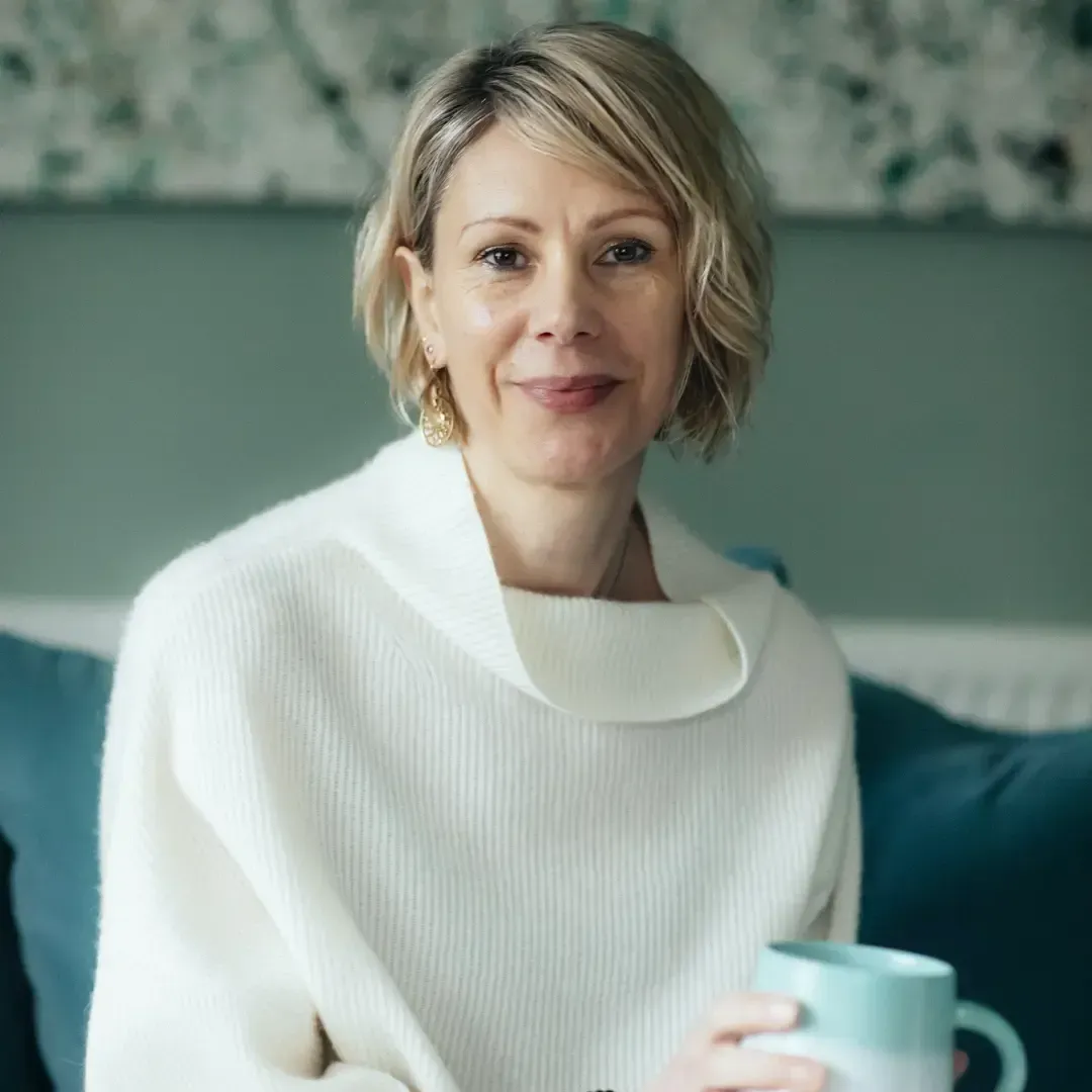 Kate sitting holding a mug and smiling at the camera