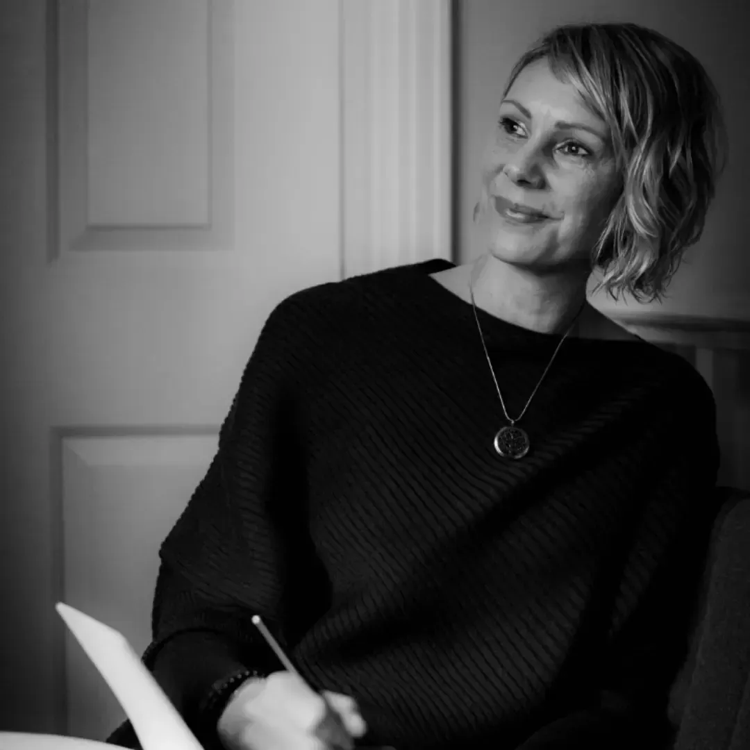 Kate in black and white seated looking away from the camera notebook on her lap