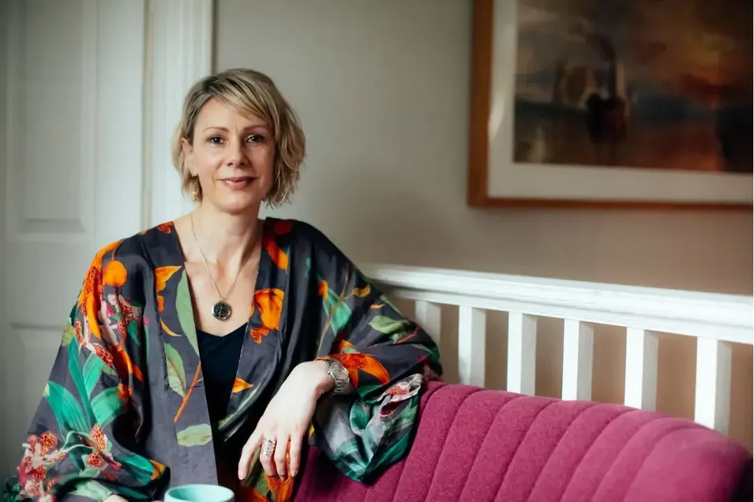 Kate on a deep pink sofa looking at the camera