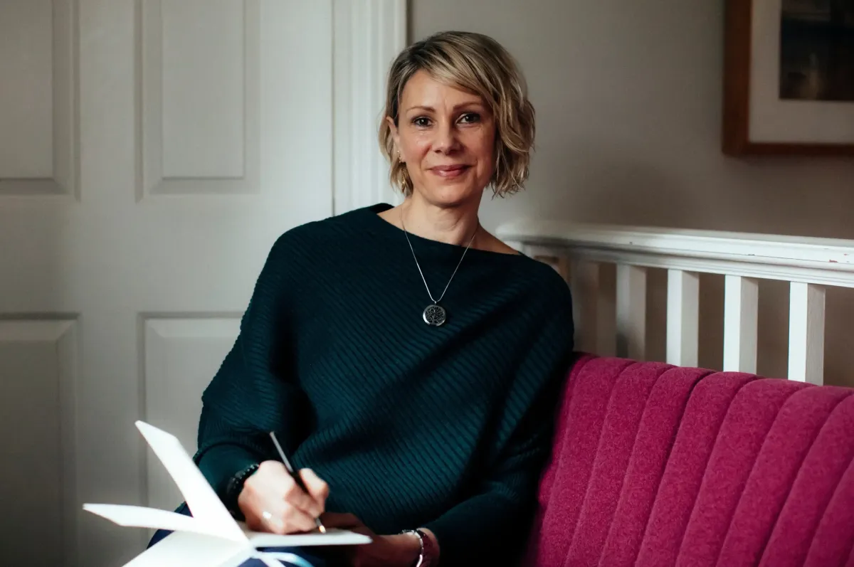 Kate sitting on a raspberry sofa with a notebook