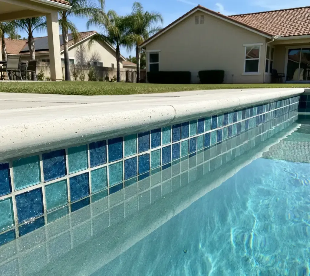 Pool cleaning tools and water test strips on a table beside a cloudy backyard swimming pool, showing pool maintenance and water chemistry testing
