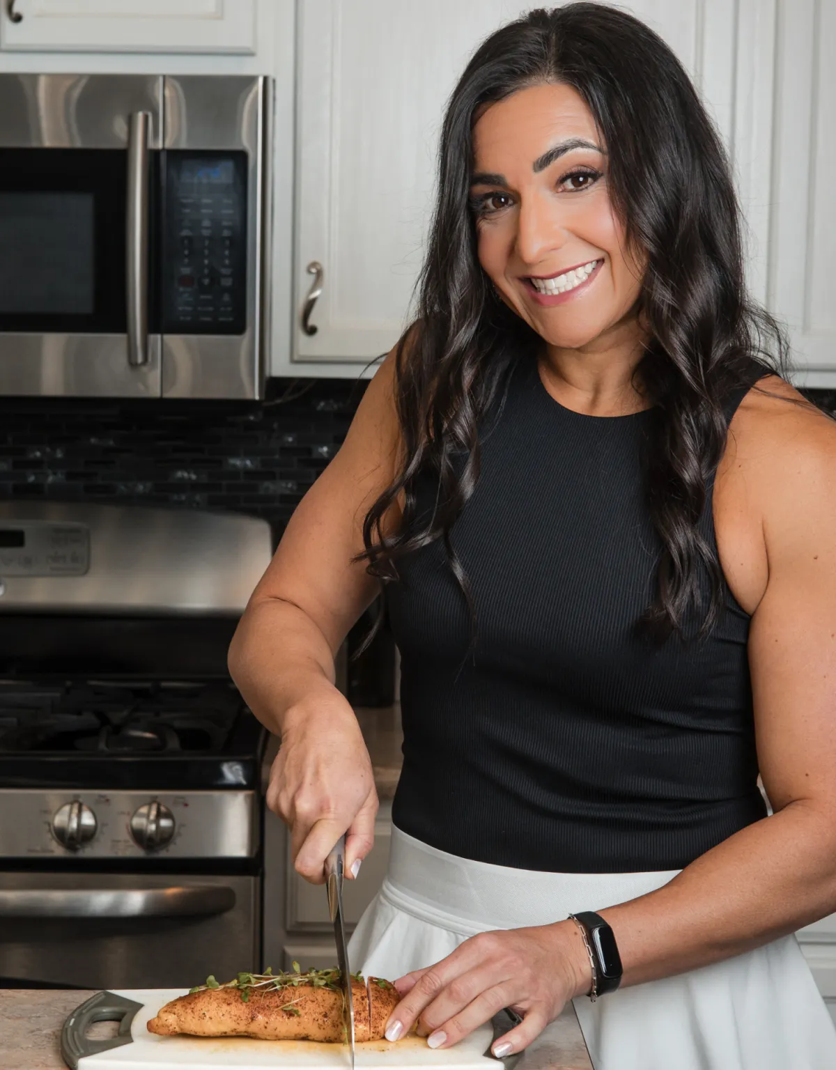 Smiling woman in a kitchen slicing chicken, representing a healthy and fulfilling lifestyle, aligned with the mission of T-REX Physical Therapy and Wellness.