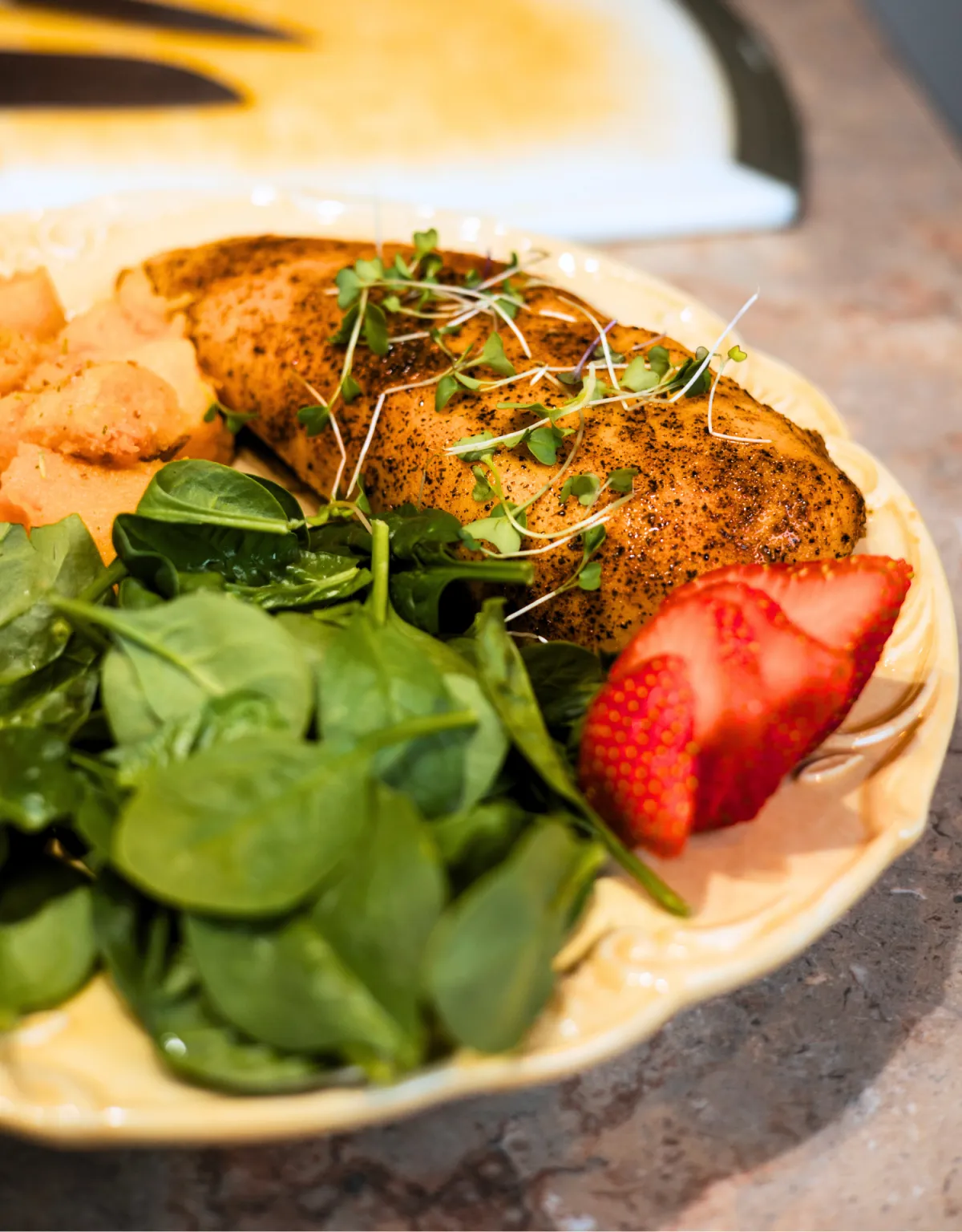 Plate of healthy food featuring seasoned chicken, fresh spinach, and sliced strawberries, emphasizing the importance of nutrition in overall wellness.