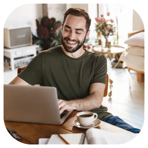 Work from home Male in his Mid  30's sitting in the comfort of his own own, working from his laptop, smiling, while enjoying coffee