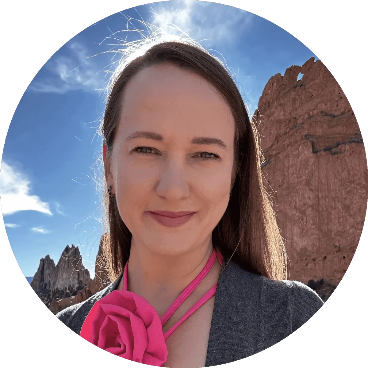 Owner of Sizzlin' Fried Ads in a pink blouse with long hair, posed outdoors with Colorado Springs mountains in the background.