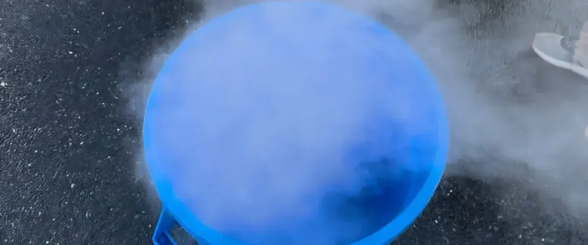 A close-up, high-angle view of a blue container filled with a thick, white, swirling fog.