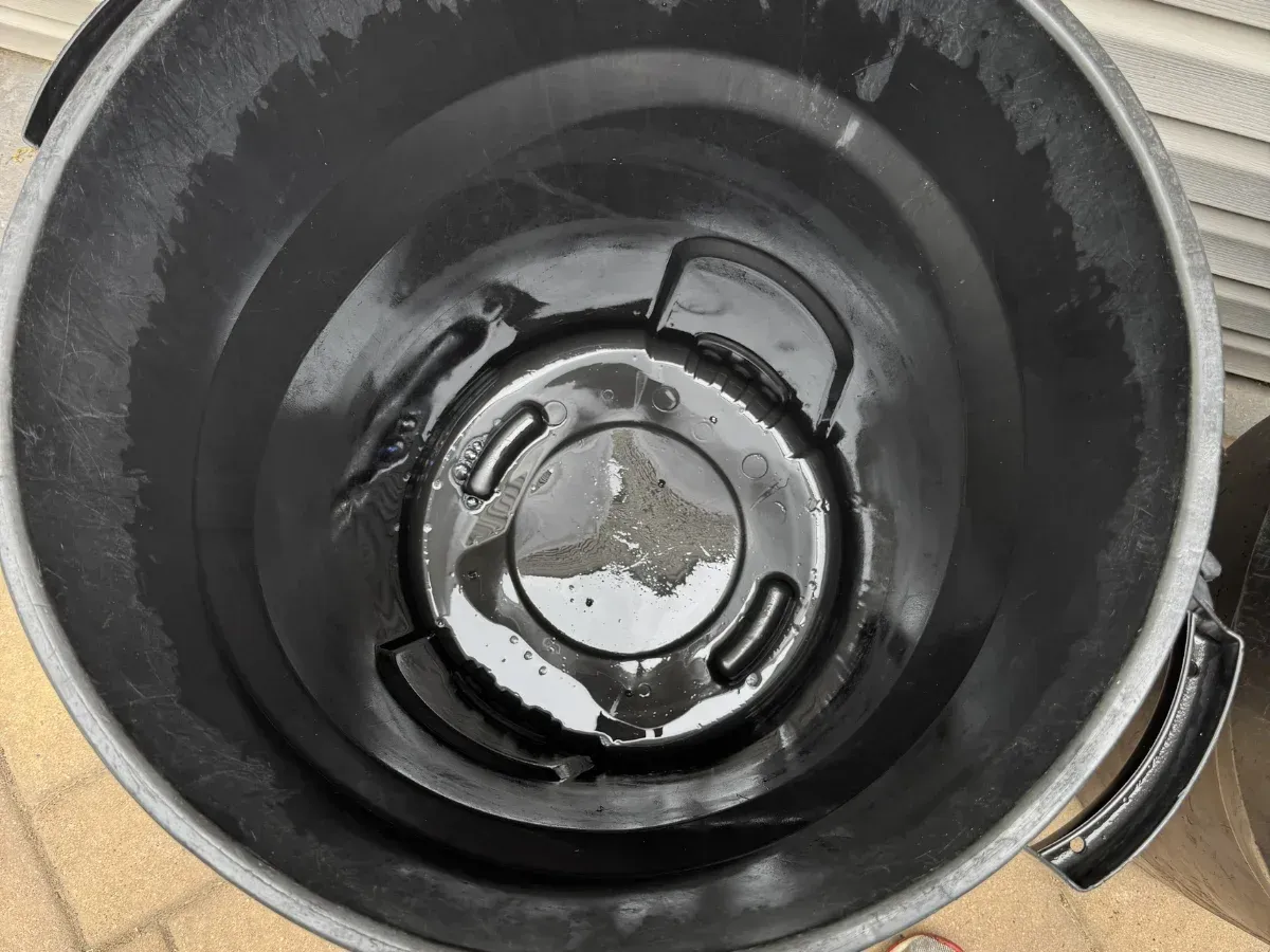 An overhead view looking into an empty, dirty black plastic garbage can outdoors on asphalt.