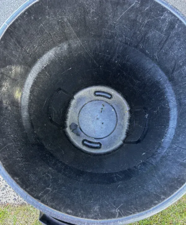 Looking down into an empty, weathered black plastic trash can with visible scratches and a dirty bottom.