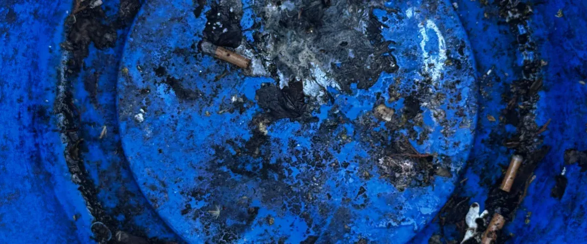 A close-up overhead shot of discarded cigarette butts and ashes in a vibrant blue barrel.