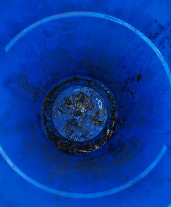 Inside a dirty, scuffed blue plastic barrel or trash can, viewed from above, with cigarette butts and ash at the bottom.