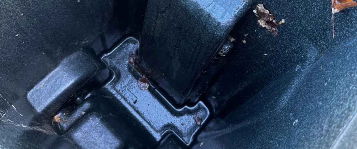 Close-up view inside a dark molded plastic container with liquid and debris at the bottom.