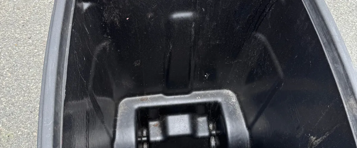 An overhead view looking inside an empty, dark, and scuffed plastic bin with some dirt on the bottom.