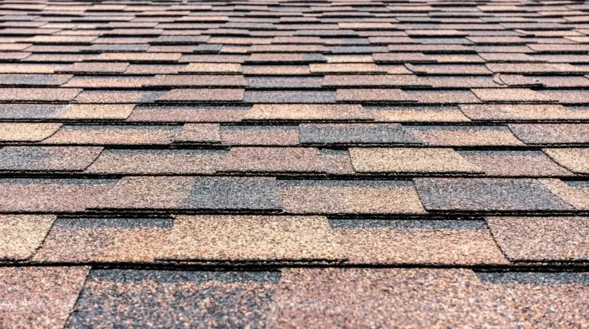 Close-up of damaged asphalt roof shingles being replaced on a residential roof during repair work.