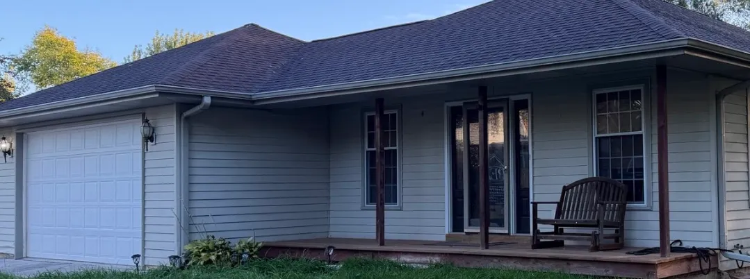A residential exterior renovation project completed by Precision Exterior Inc., featuring a house with updated siding, a new roof, and a welcoming front porch with a wooden bench.