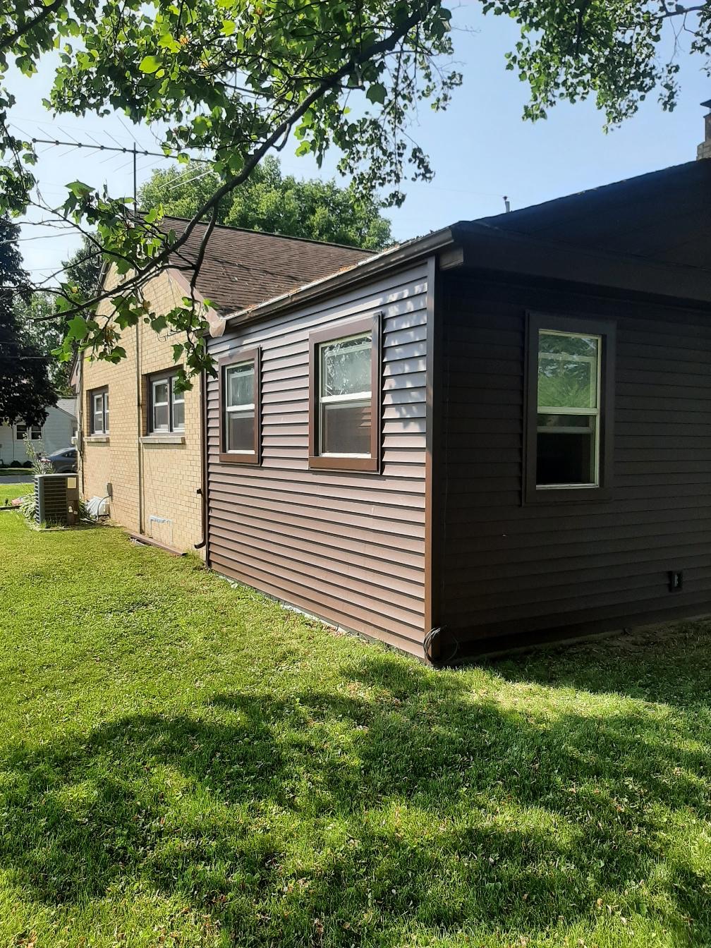 A residential home exterior renovation by Precision Exterior Inc. in Lena, IL. The image features newly installed dark brown horizontal vinyl siding with matching dark brown window trim on a new addition. This dark siding is precisely integrated against the existing light-colored brick structure, completed by our expert siding installation team serving Lena and surrounding areas.