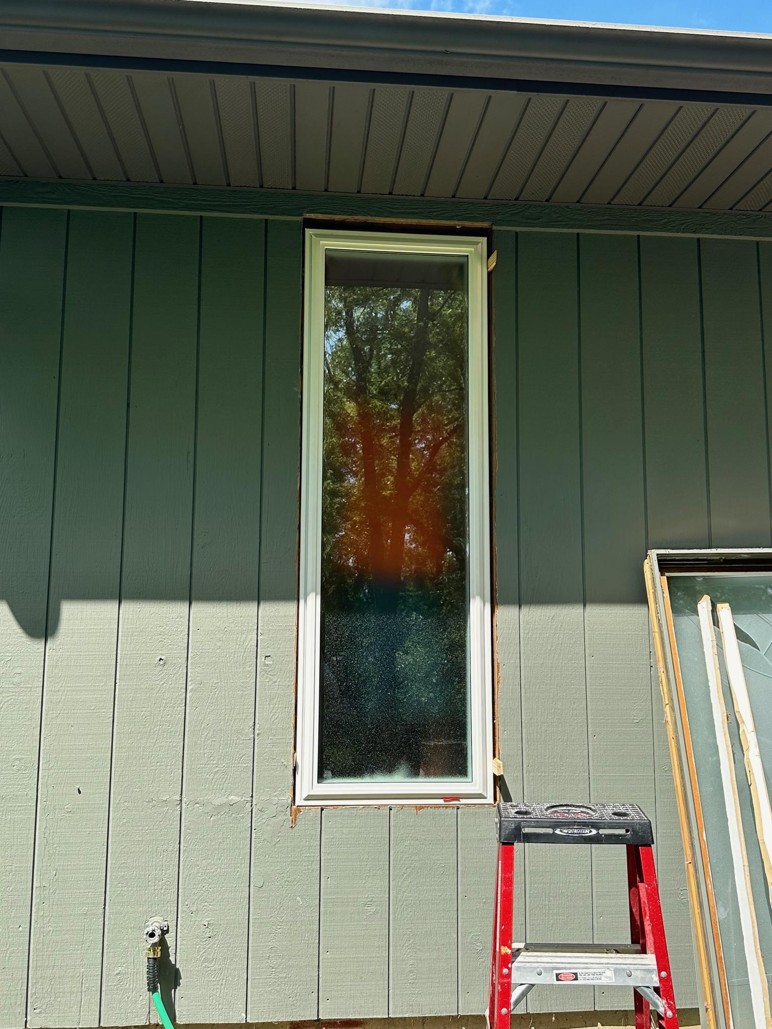 New white vinyl window unit installed on a house with dark siding.
