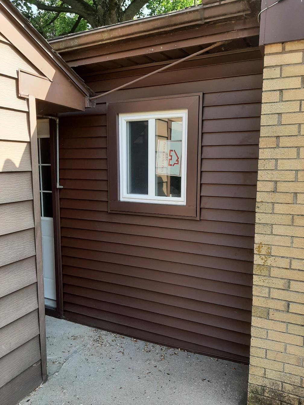 A residential home exterior featuring newly installed dark brown horizontal vinyl siding with a matching dark brown window trim. A new white vinyl sliding window is shown installed cleanly into the siding by Precision Exterior Inc., serving Lena, IL and surrounding areas.
