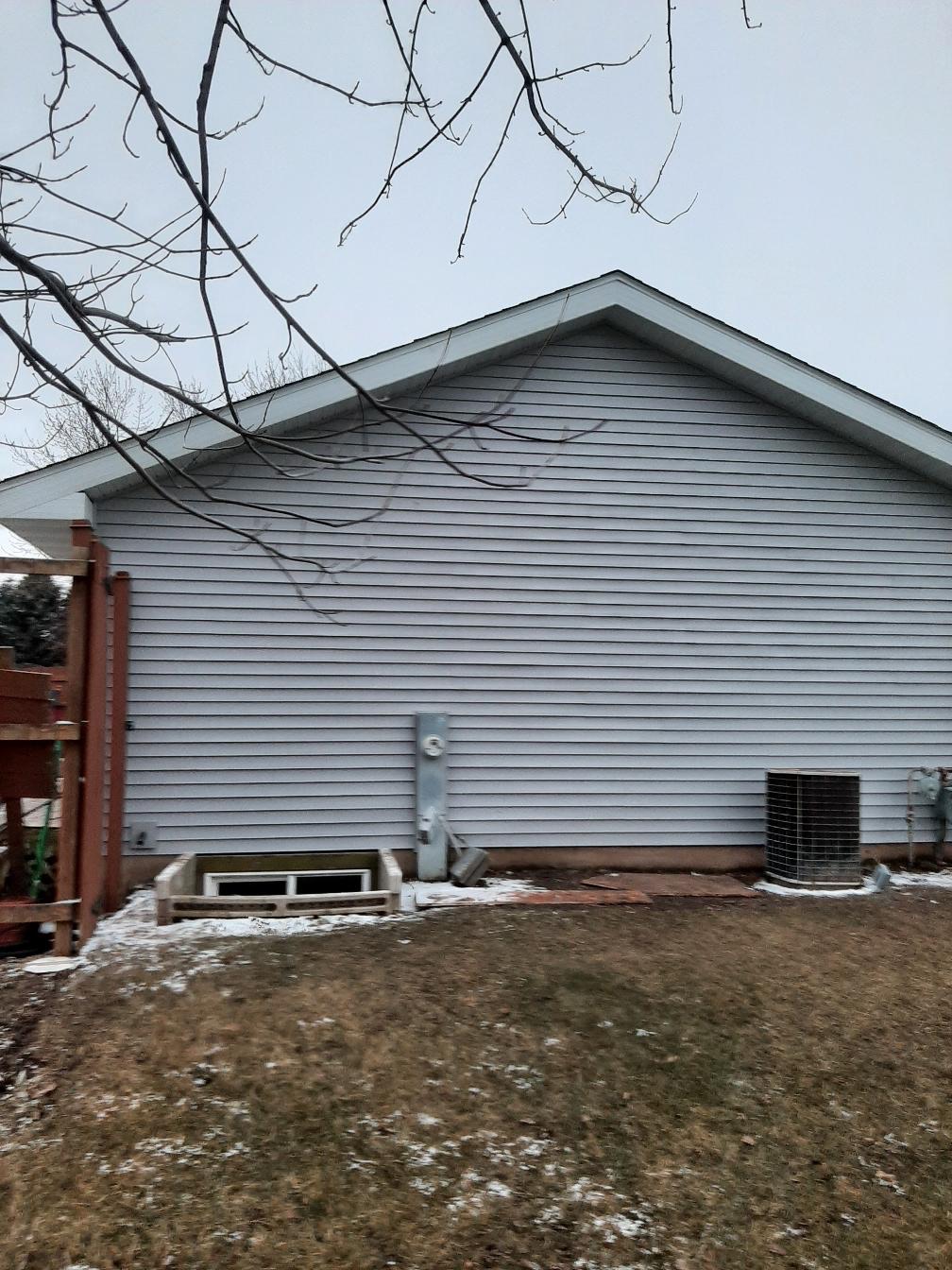 A residential home showcasing clean, newly installed light gray horizontal vinyl siding on a gable wall. Work completed by Precision Exterior Inc., serving Lena, IL and surrounding areas. The image shows the side of the house under an overcast sky, highlighting precision siding installation, trim details, and foundation integration.