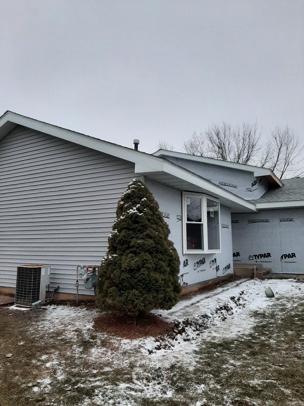 A residential home siding installation in progress by Precision Exterior Inc. in Lena, IL. The image features a finished gable section with light gray horizontal vinyl siding juxtaposed against adjacent walls wrapped in TYPAR weather barrier, showing the professional installation process.