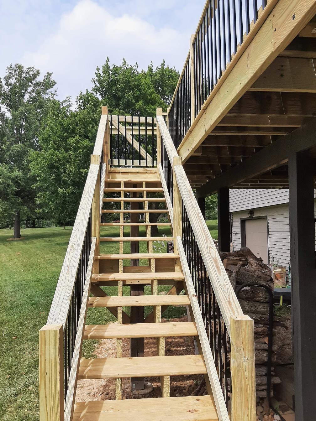 Custom pressure-treated wood deck staircase with black metal spindle railings and a top safety gate built by Precision Exterior Inc.