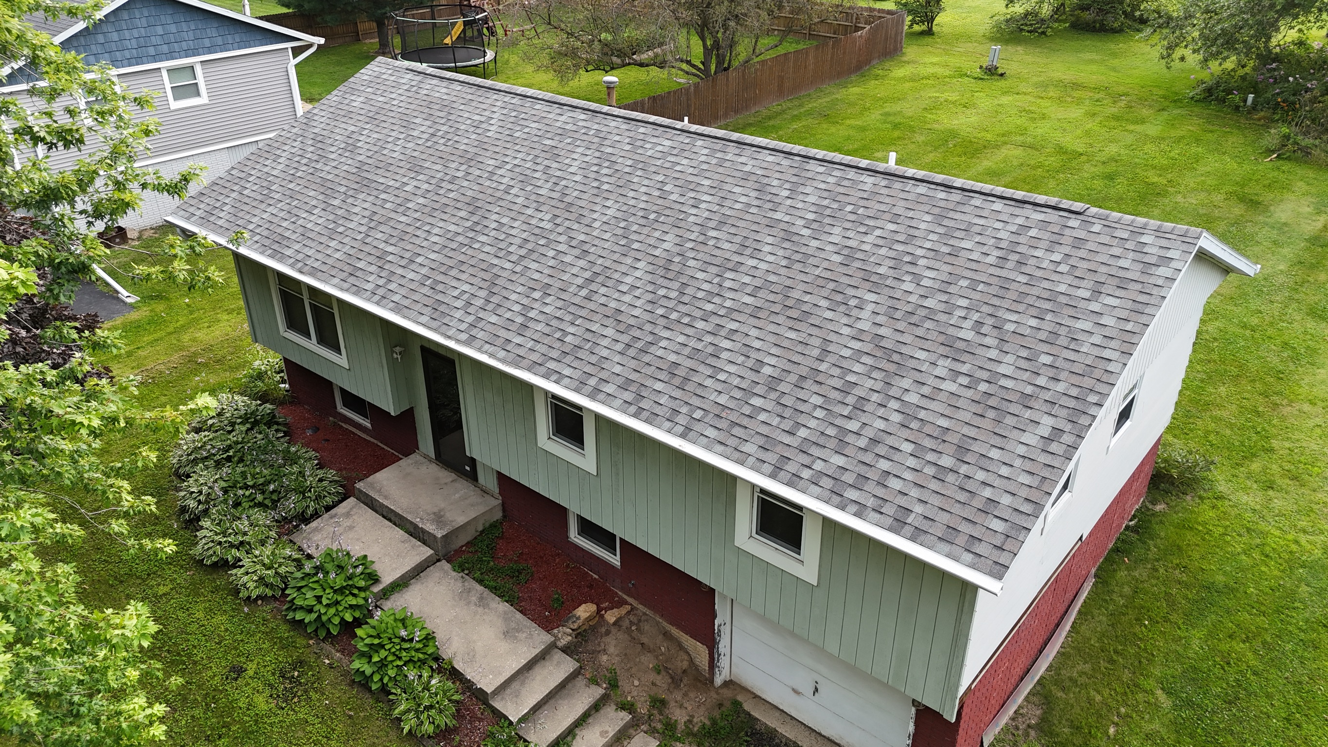 Drone view of a long, single-story residential roof with new shingles.