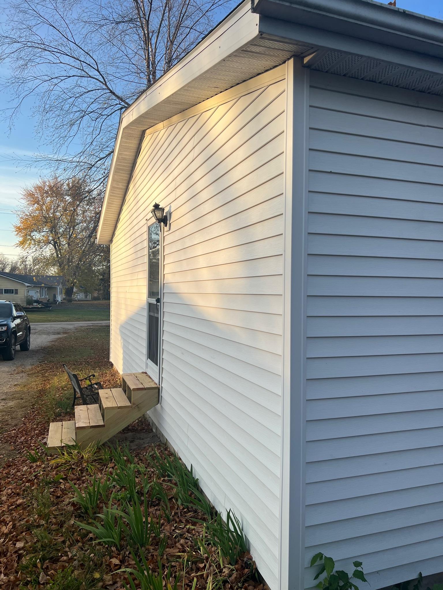 Custom pressure-treated wood exterior entry stairs installed on a house with white vinyl siding by Precision Exterior Inc.