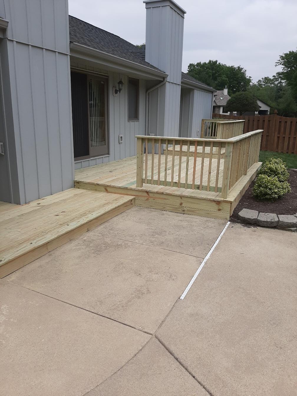 Custom residential multi-level pressure-treated wood deck with wood safety railings built next to a concrete patio by Precision Exterior Inc.