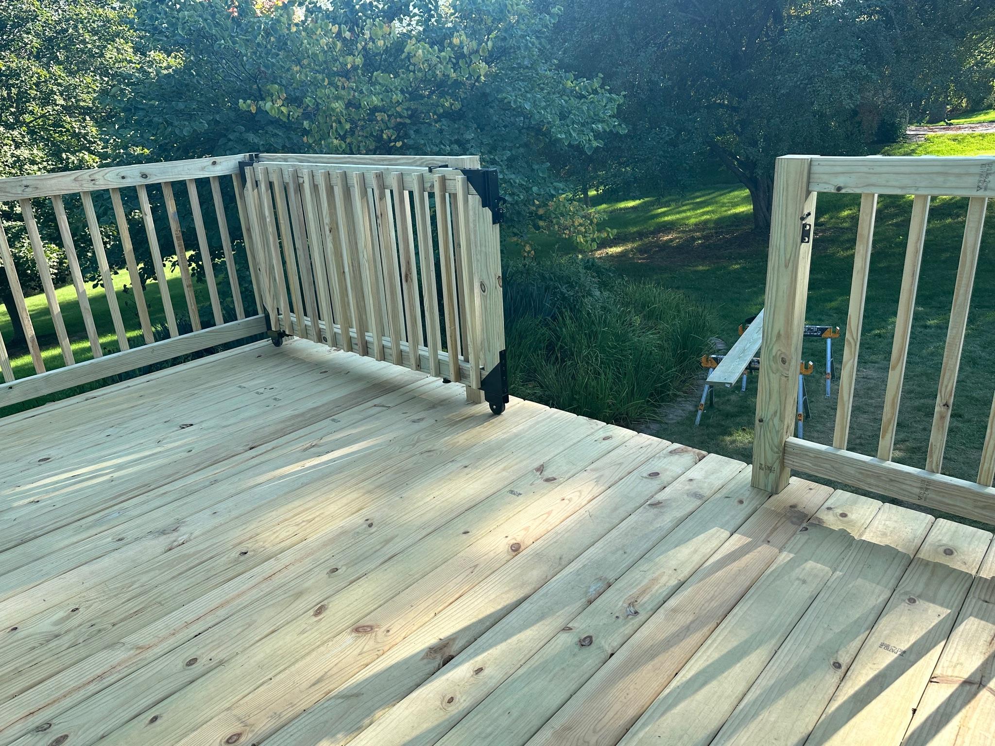 Custom wooden deck safety gate with black hardware and wheel built by Precision Exterior Inc. on a residential backyard deck in Lena, IL.