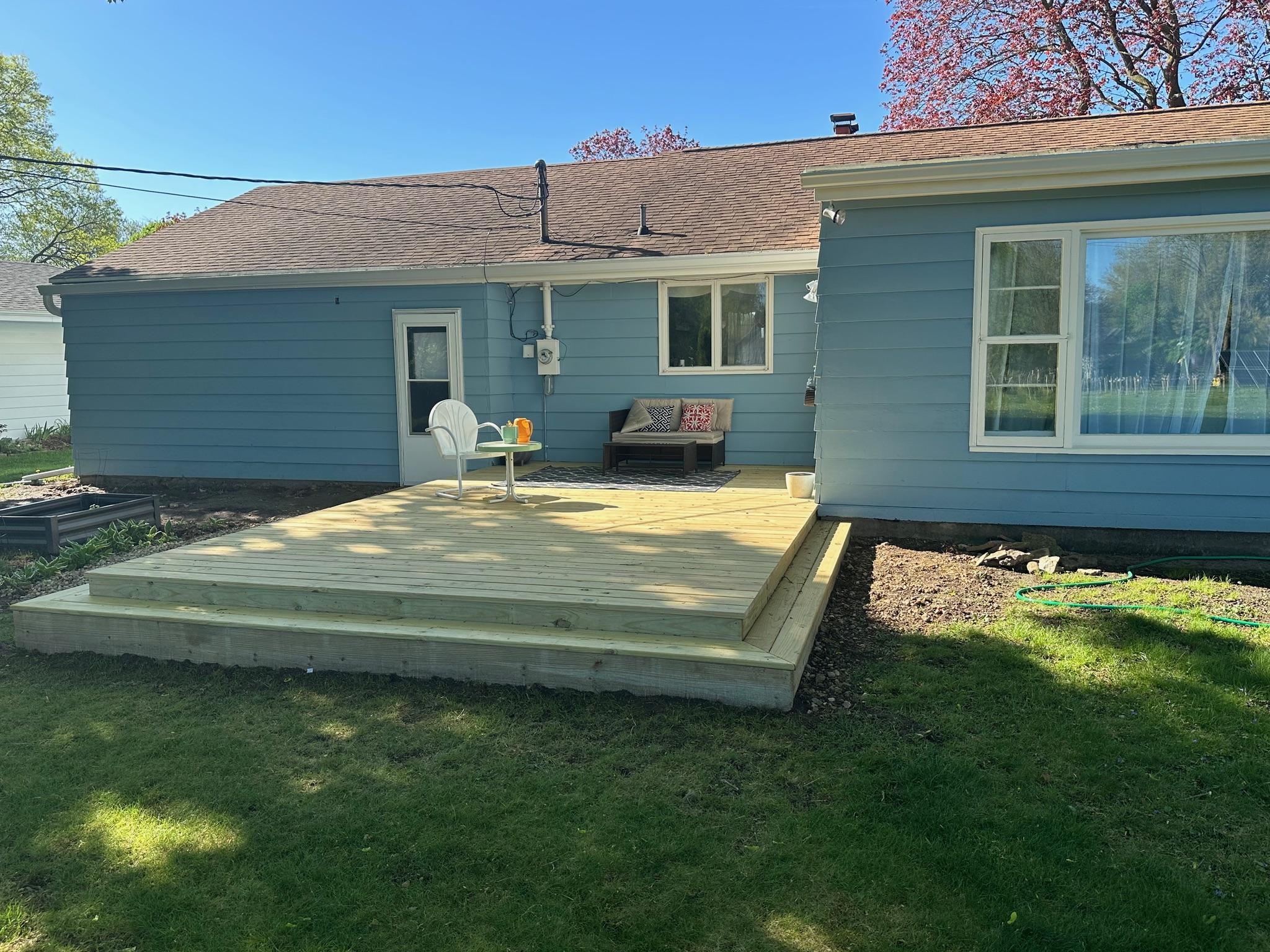 Custom ground-level pressure-treated wood patio deck with step-down stairs built on a blue house by Precision Exterior Inc.