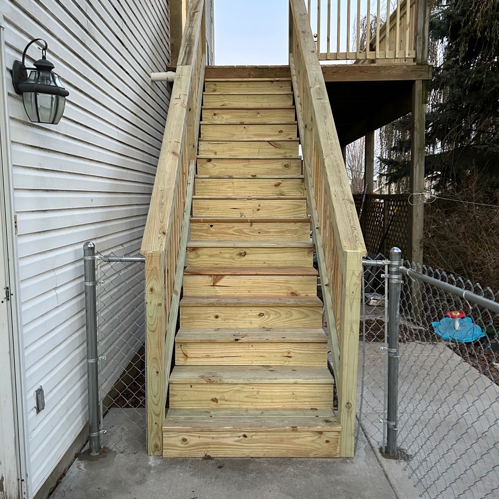 Custom pressure-treated wood deck staircase with solid wooden safety handrails built next to a residential home by Precision Exterior Inc.