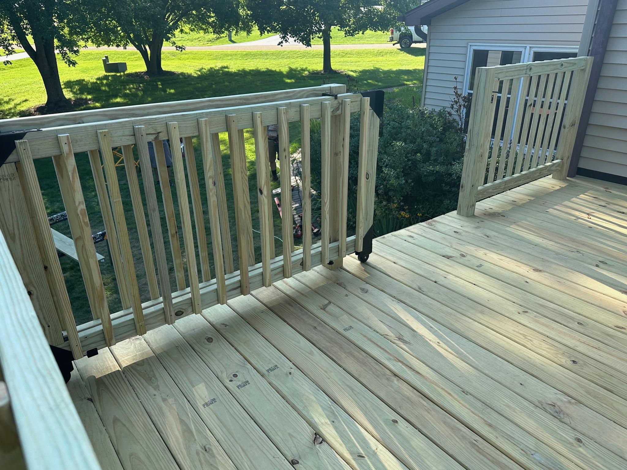 Custom pressure-treated wood deck with a built-in safety gate and railings completed by Precision Exterior Inc.